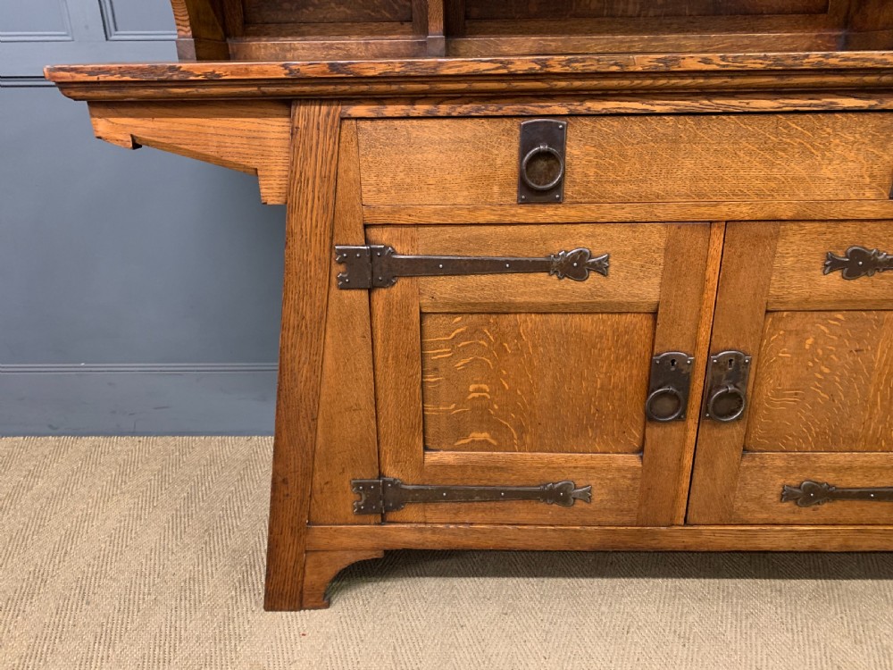 An Arts and Crafts period oak dresser featuring leaded glass upper cabinet doors, open side shelves, metal strap hinges, and a lower two-door cupboard. View VIII