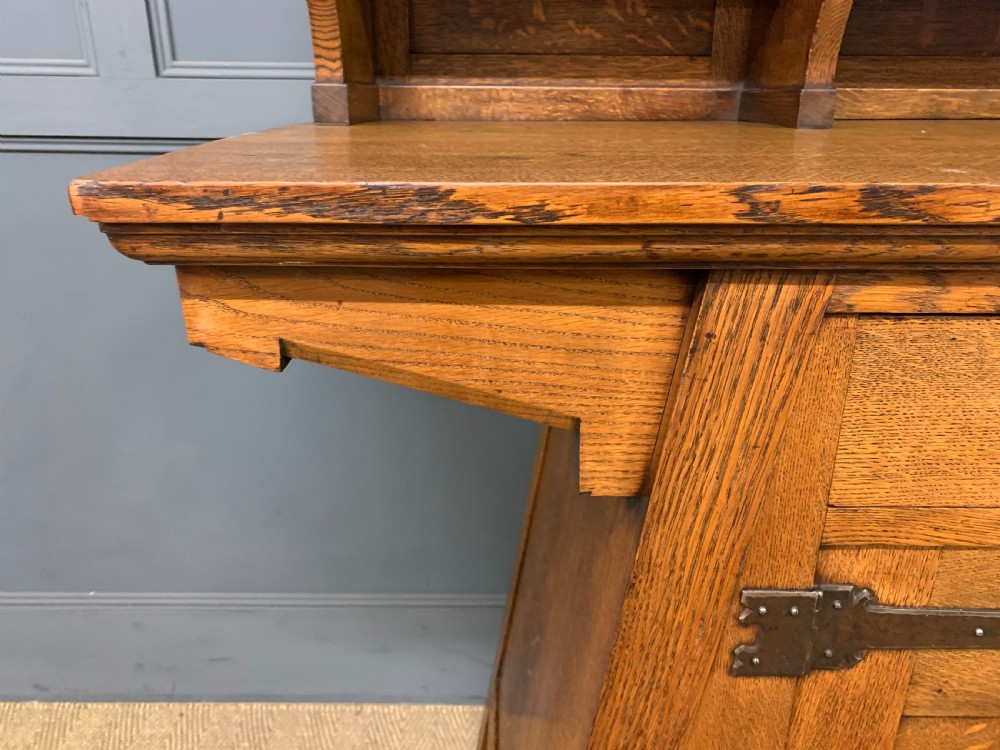 An Arts and Crafts period oak dresser featuring leaded glass upper cabinet doors, open side shelves, metal strap hinges, and a lower two-door cupboard. View IX
