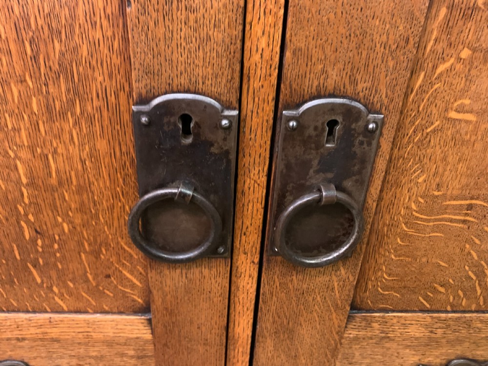 An Arts and Crafts period oak dresser featuring leaded glass upper cabinet doors, open side shelves, metal strap hinges, and a lower two-door cupboard. View XI