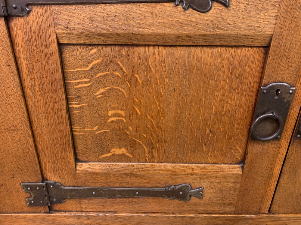 An Arts and Crafts period oak dresser featuring leaded glass upper cabinet doors, open side shelves, metal strap hinges, and a lower two-door cupboard. View XII