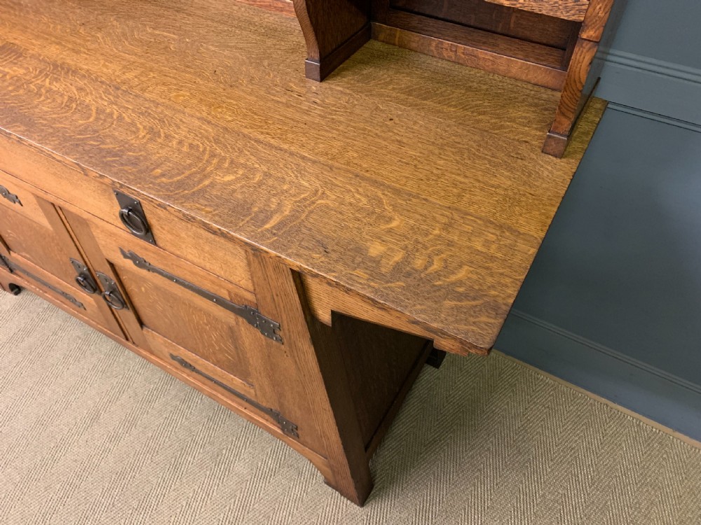An Arts and Crafts period oak dresser featuring leaded glass upper cabinet doors, open side shelves, metal strap hinges, and a lower two-door cupboard. View XV