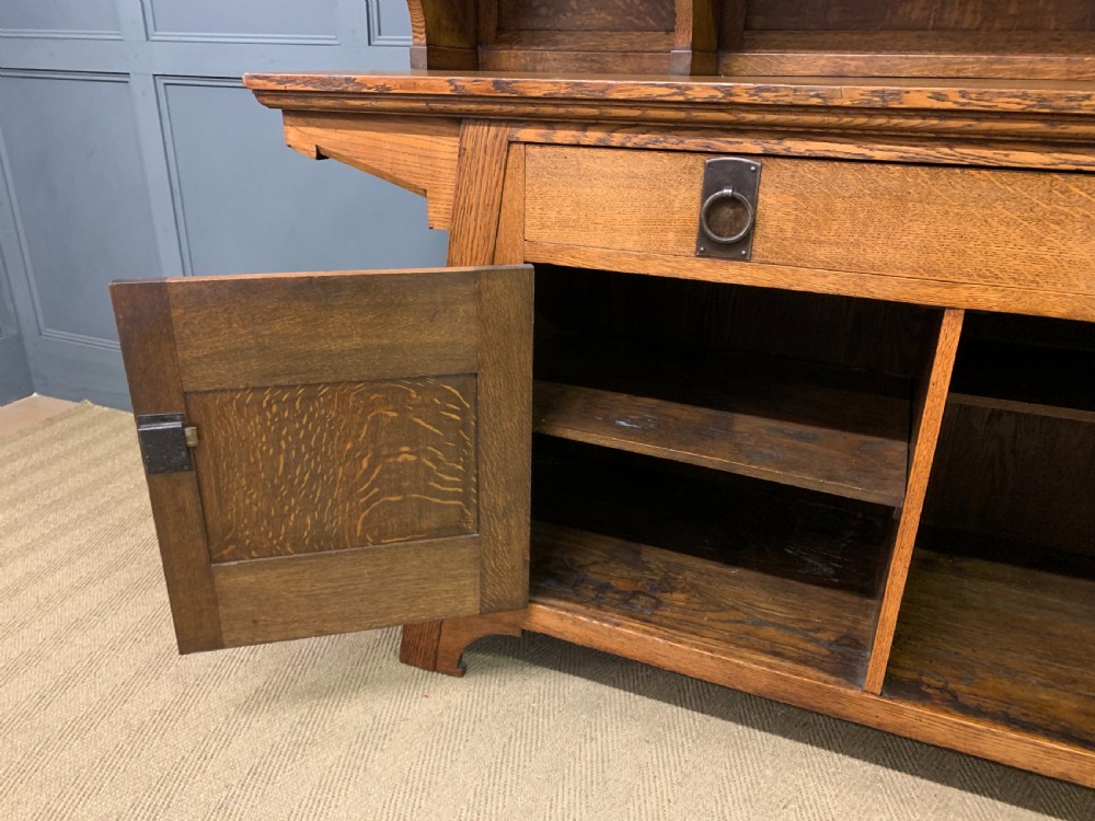 An Arts and Crafts period oak dresser featuring leaded glass upper cabinet doors, open side shelves, metal strap hinges, and a lower two-door cupboard. View XVIII