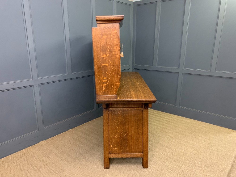 An Arts and Crafts period oak dresser featuring leaded glass upper cabinet doors, open side shelves, metal strap hinges, and a lower two-door cupboard. View XX