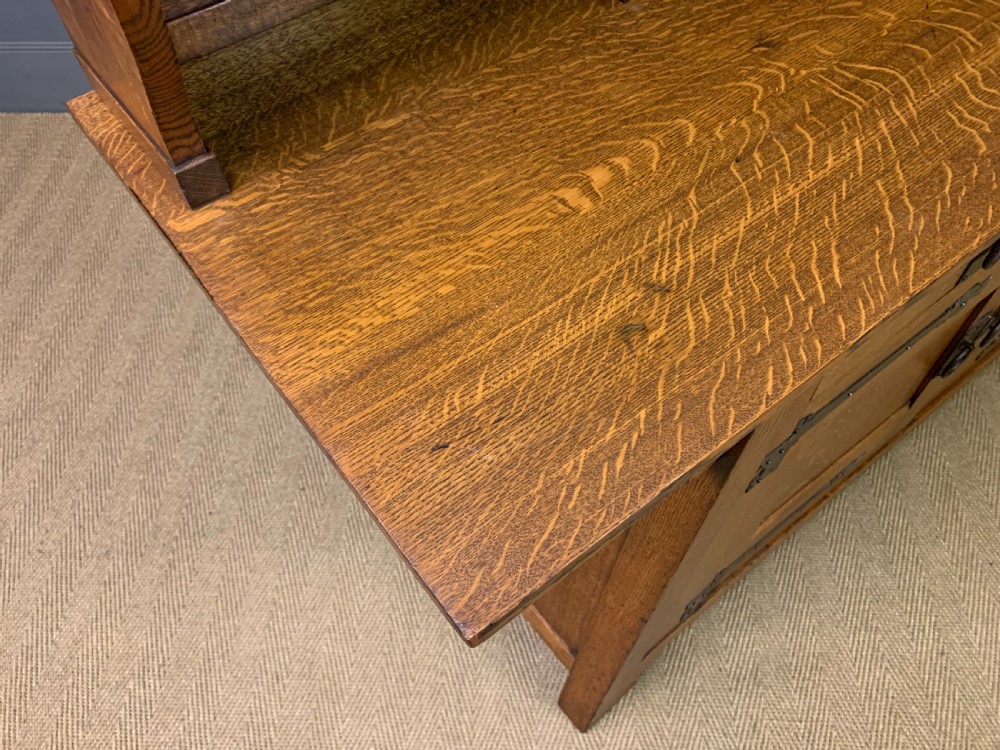 An Arts and Crafts period oak dresser featuring leaded glass upper cabinet doors, open side shelves, metal strap hinges, and a lower two-door cupboard. View XXI