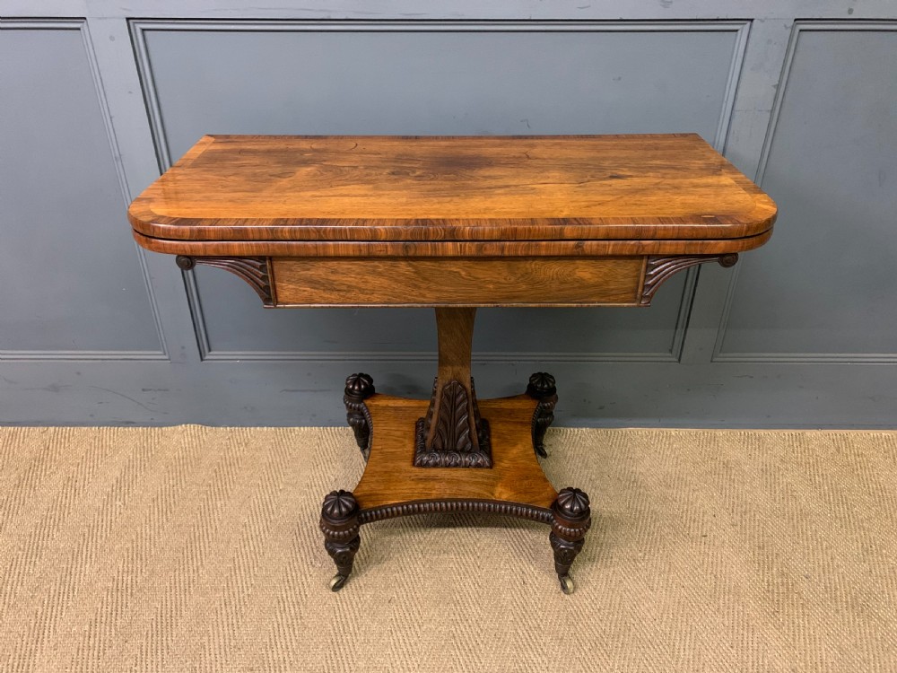 A Regency period rosewood fold-over card table with a swivel top, a central pedestal support, and a concave platform base resting on carved feet with brass castors.