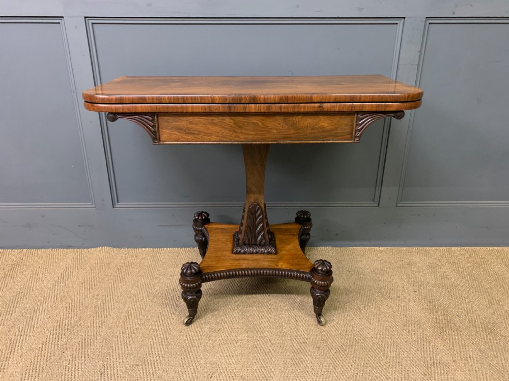 A Regency period rosewood fold-over card table with a swivel top, a central pedestal support, and a concave platform base resting on carved feet with brass castors. View II