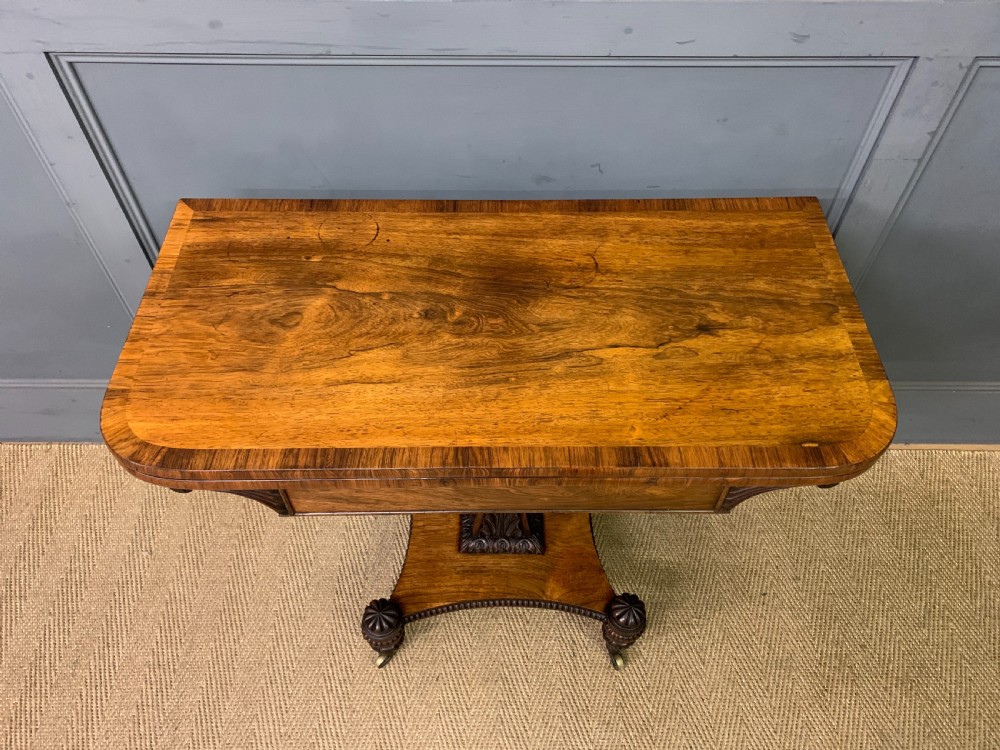 A Regency period rosewood fold-over card table with a swivel top, a central pedestal support, and a concave platform base resting on carved feet with brass castors. View III