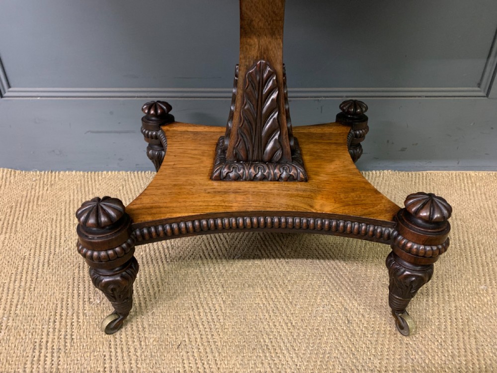 A Regency period rosewood fold-over card table with a swivel top, a central pedestal support, and a concave platform base resting on carved feet with brass castors. View IV