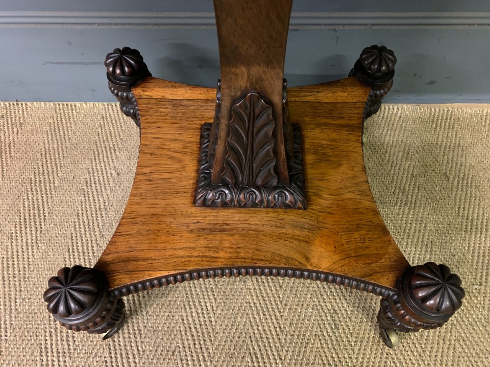 A Regency period rosewood fold-over card table with a swivel top, a central pedestal support, and a concave platform base resting on carved feet with brass castors. View VII