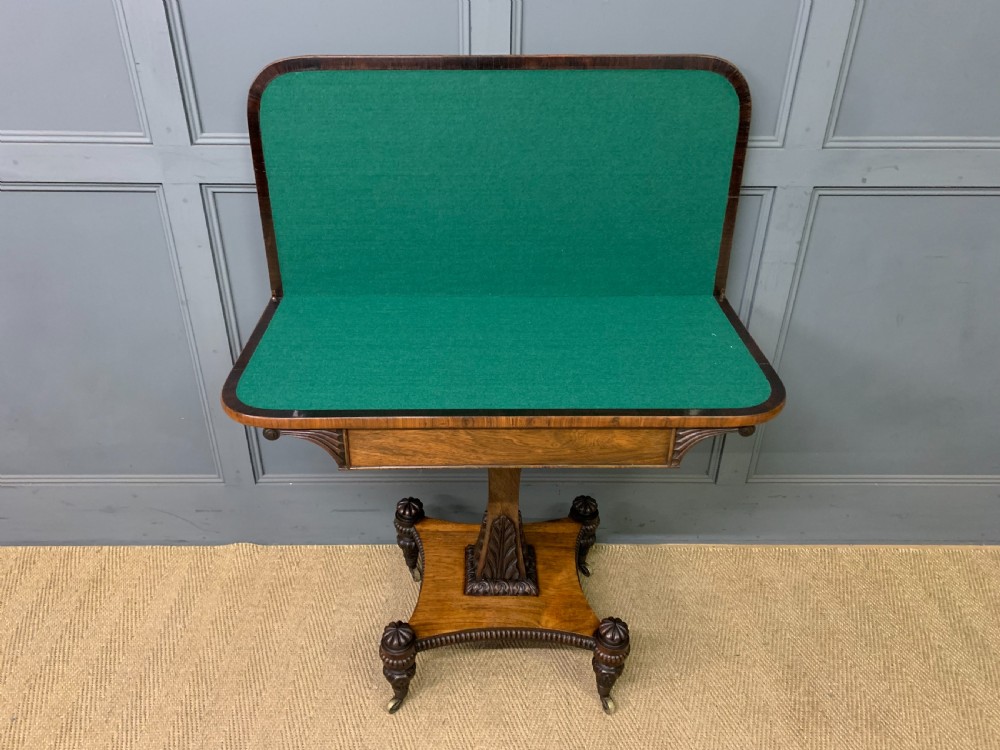 A Regency period rosewood fold-over card table with a swivel top, a central pedestal support, and a concave platform base resting on carved feet with brass castors. View IX