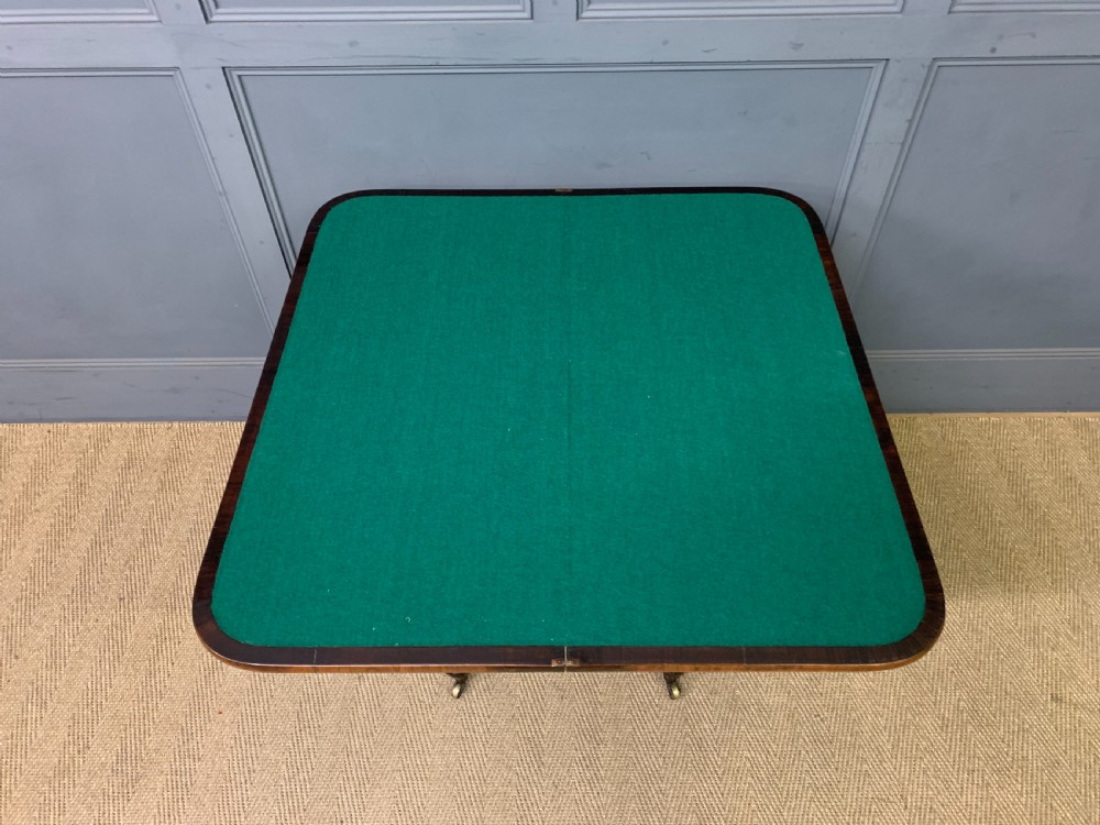 A Regency period rosewood fold-over card table with a swivel top, a central pedestal support, and a concave platform base resting on carved feet with brass castors. View XII