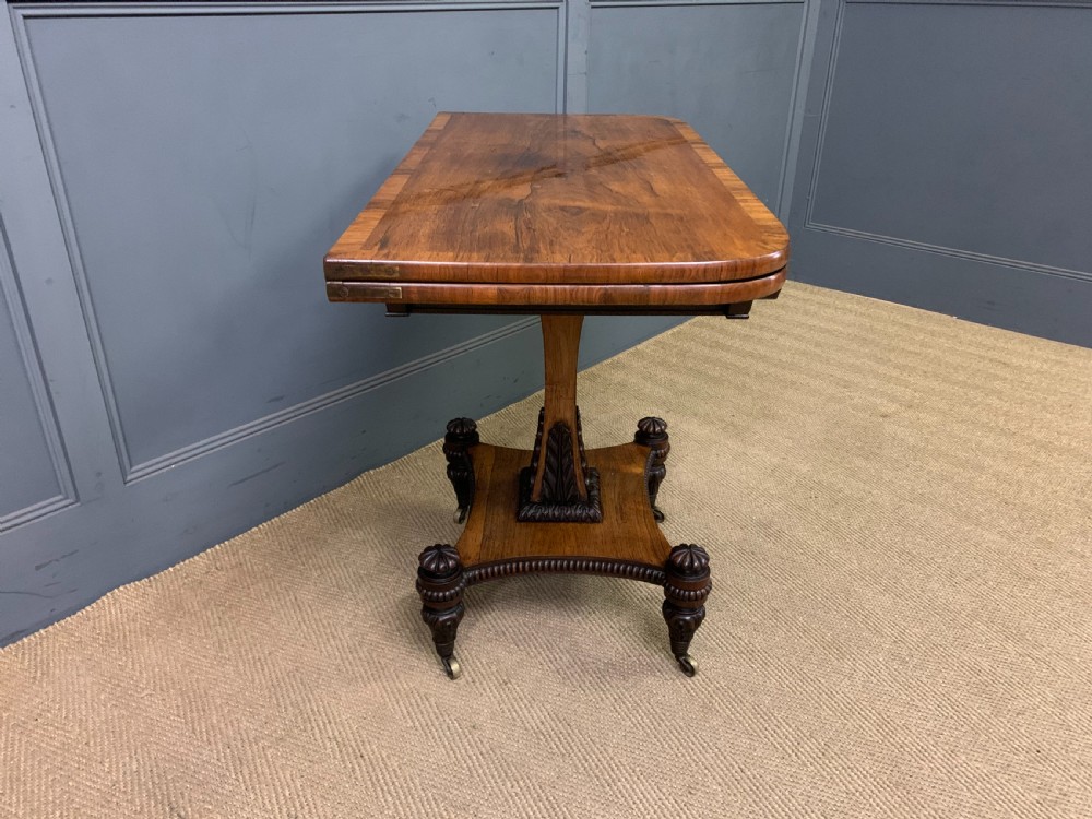 A Regency period rosewood fold-over card table with a swivel top, a central pedestal support, and a concave platform base resting on carved feet with brass castors. View XV