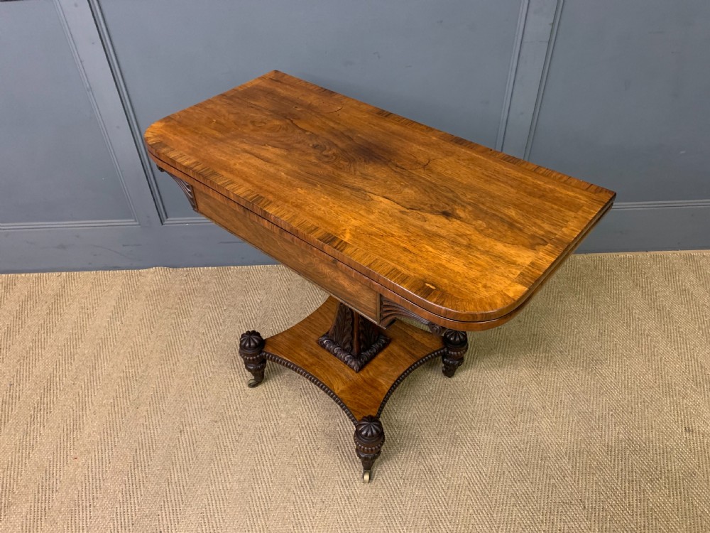 A Regency period rosewood fold-over card table with a swivel top, a central pedestal support, and a concave platform base resting on carved feet with brass castors. View XVI