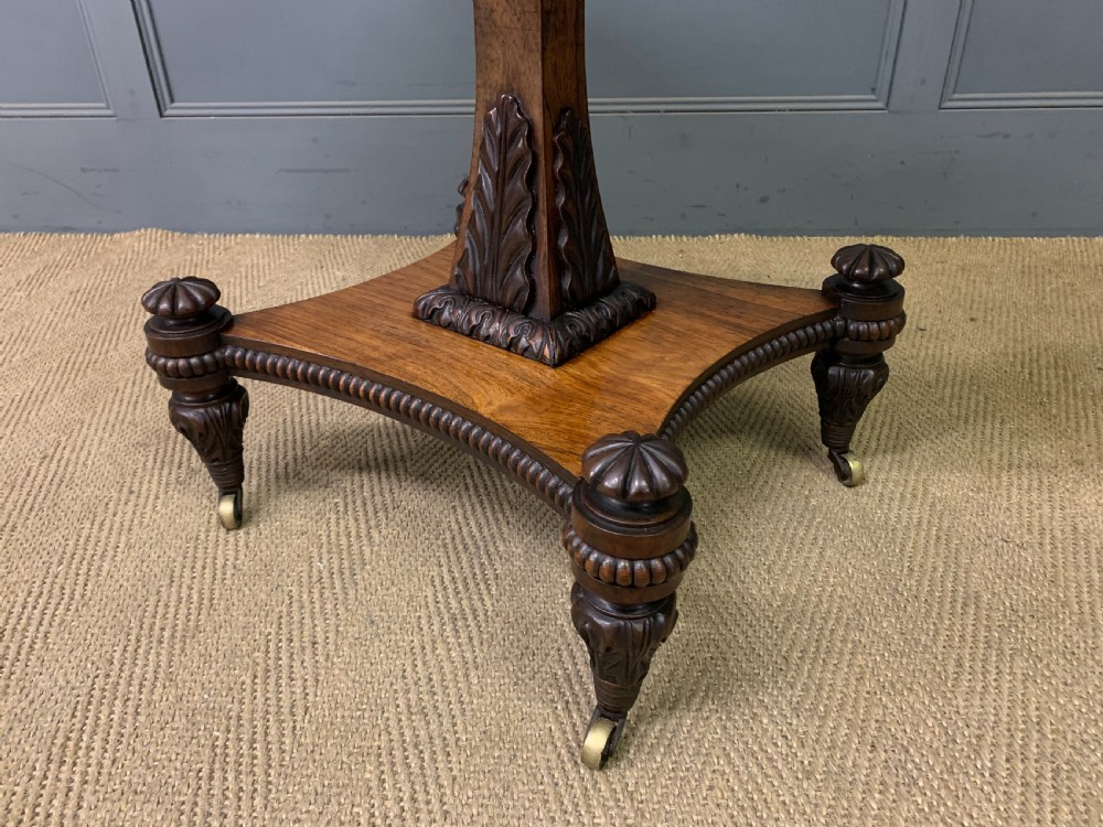 A Regency period rosewood fold-over card table with a swivel top, a central pedestal support, and a concave platform base resting on carved feet with brass castors. View XVII