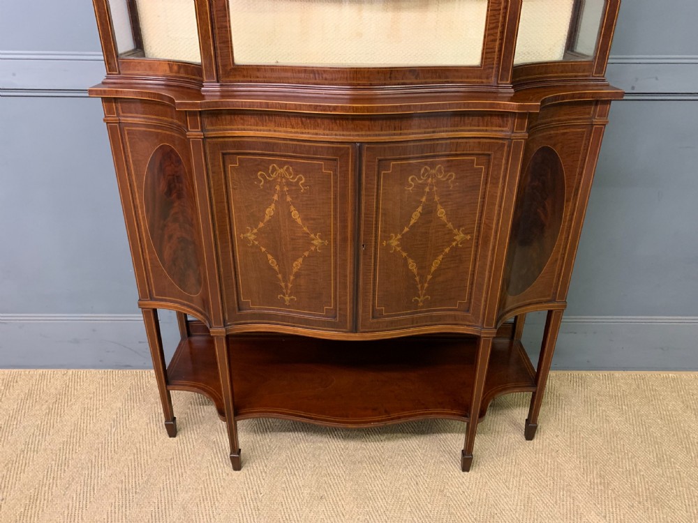 An Edwardian inlaid mahogany display cabinet featuring a glazed upper section, bow-front lower doors with marquetry panels, and tapered legs with a lower shelf. View II