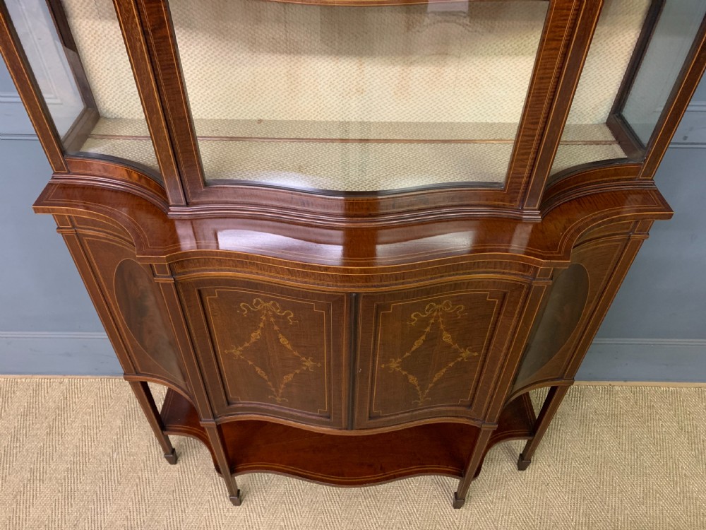 An Edwardian inlaid mahogany display cabinet featuring a glazed upper section, bow-front lower doors with marquetry panels, and tapered legs with a lower shelf. View III