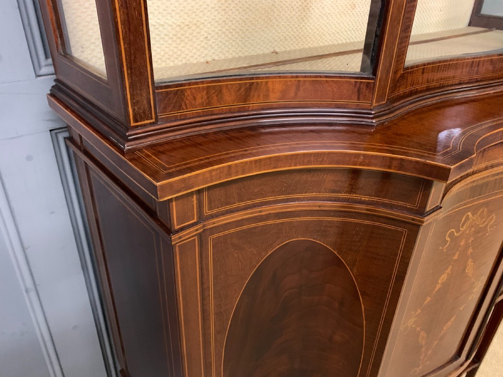 An Edwardian inlaid mahogany display cabinet featuring a glazed upper section, bow-front lower doors with marquetry panels, and tapered legs with a lower shelf. View VII