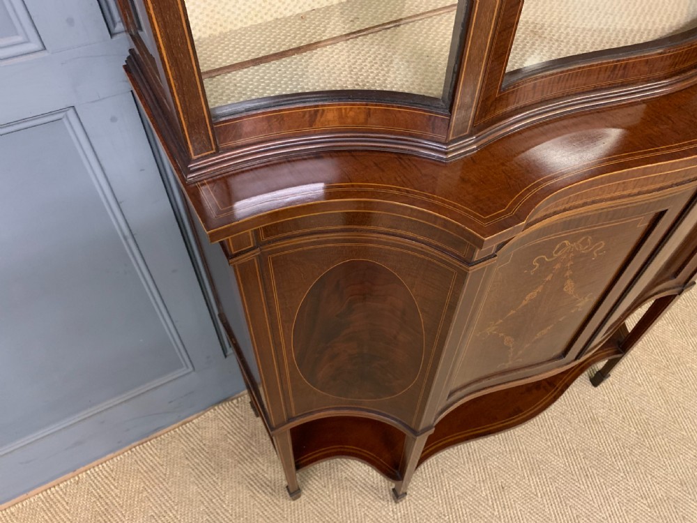 An Edwardian inlaid mahogany display cabinet featuring a glazed upper section, bow-front lower doors with marquetry panels, and tapered legs with a lower shelf. View VIII
