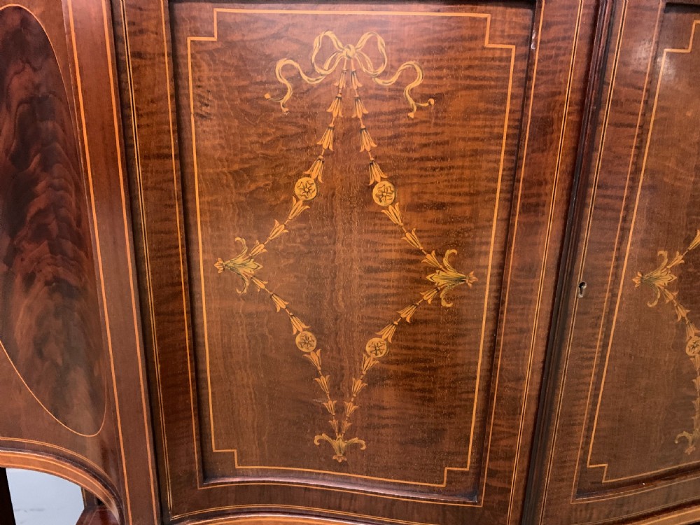 An Edwardian inlaid mahogany display cabinet featuring a glazed upper section, bow-front lower doors with marquetry panels, and tapered legs with a lower shelf. View XI