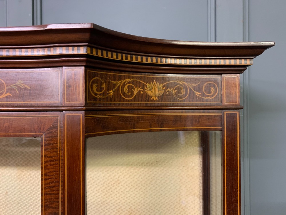 An Edwardian inlaid mahogany display cabinet featuring a glazed upper section, bow-front lower doors with marquetry panels, and tapered legs with a lower shelf. View XIV