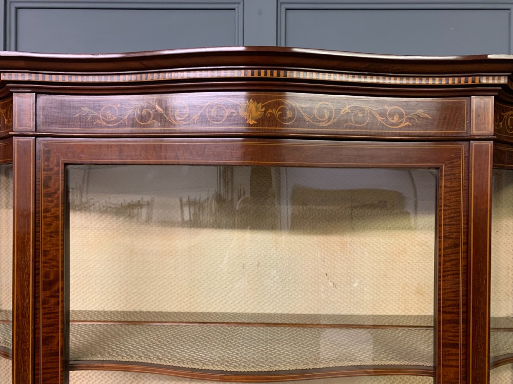 An Edwardian inlaid mahogany display cabinet featuring a glazed upper section, bow-front lower doors with marquetry panels, and tapered legs with a lower shelf. View XV
