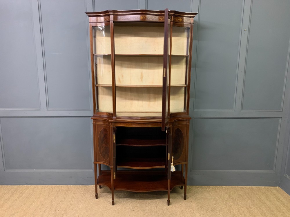 An Edwardian inlaid mahogany display cabinet featuring a glazed upper section, bow-front lower doors with marquetry panels, and tapered legs with a lower shelf. View XVIII