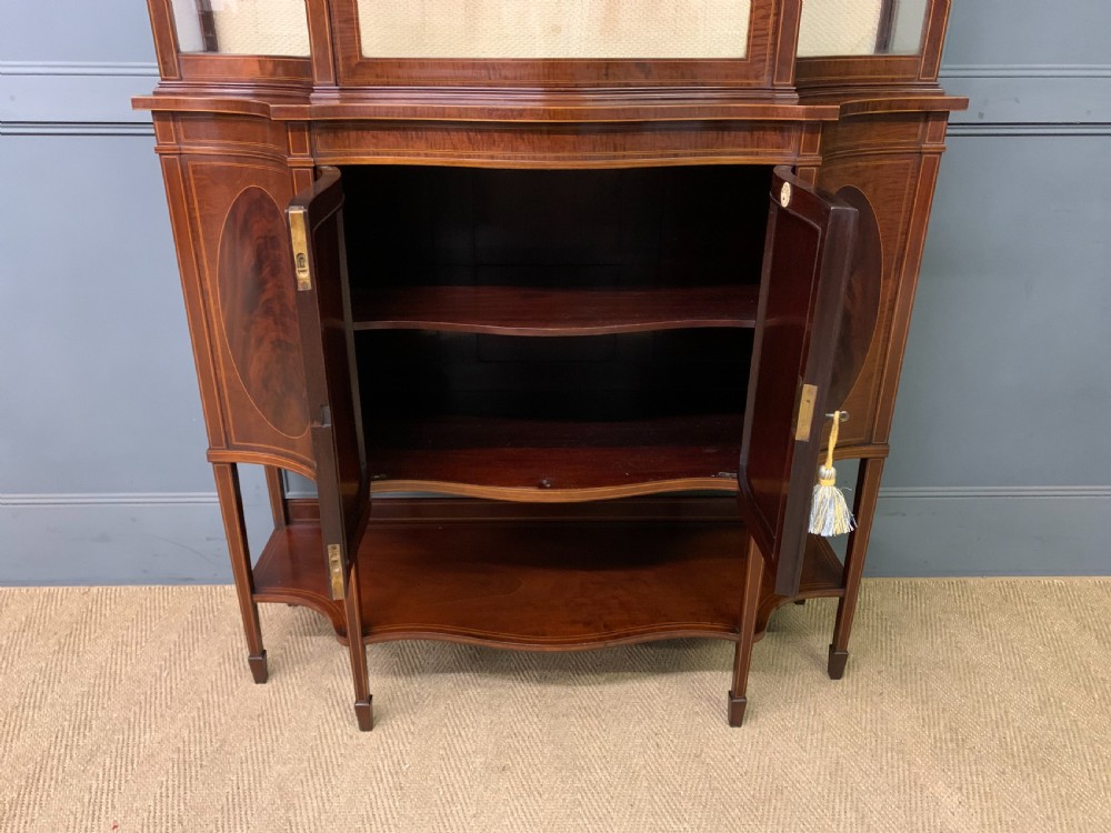 An Edwardian inlaid mahogany display cabinet featuring a glazed upper section, bow-front lower doors with marquetry panels, and tapered legs with a lower shelf. View XIX