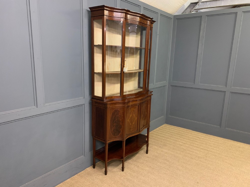An Edwardian inlaid mahogany display cabinet featuring a glazed upper section, bow-front lower doors with marquetry panels, and tapered legs with a lower shelf. View XXI