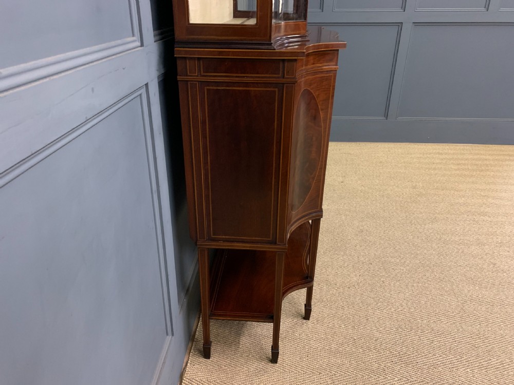 An Edwardian inlaid mahogany display cabinet featuring a glazed upper section, bow-front lower doors with marquetry panels, and tapered legs with a lower shelf. View XXII