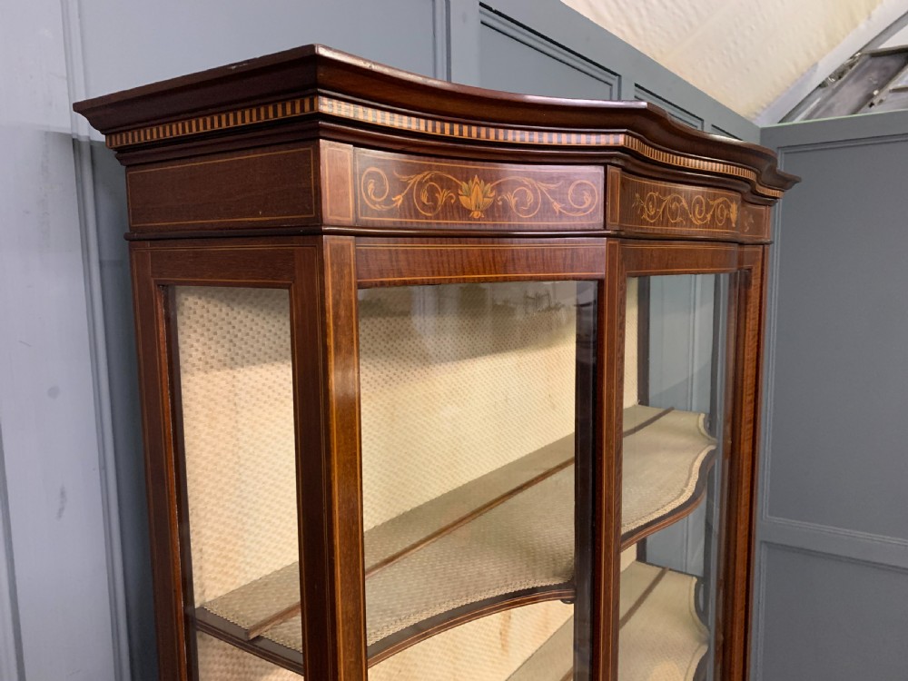 An Edwardian inlaid mahogany display cabinet featuring a glazed upper section, bow-front lower doors with marquetry panels, and tapered legs with a lower shelf. View XXIV