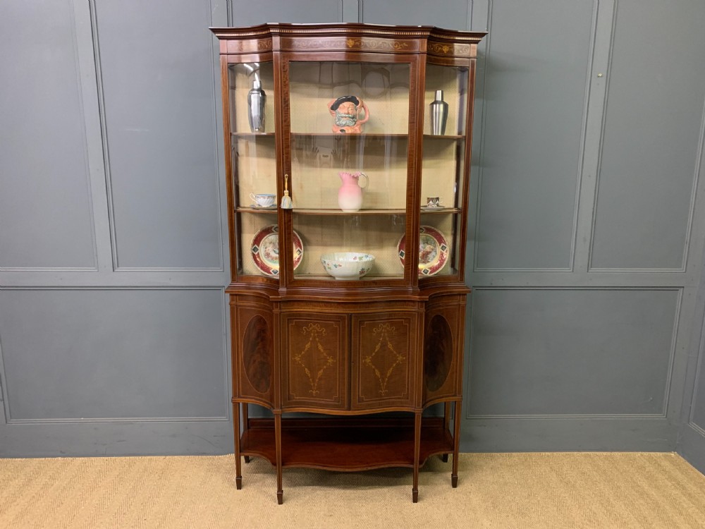 An Edwardian inlaid mahogany display cabinet featuring a glazed upper section, bow-front lower doors with marquetry panels, and tapered legs with a lower shelf. View XXV