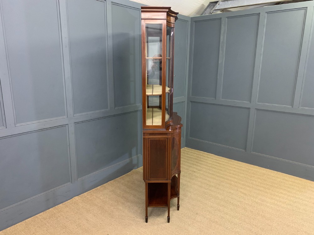 An Edwardian inlaid mahogany display cabinet featuring a glazed upper section, bow-front lower doors with marquetry panels, and tapered legs with a lower shelf. View XXVII