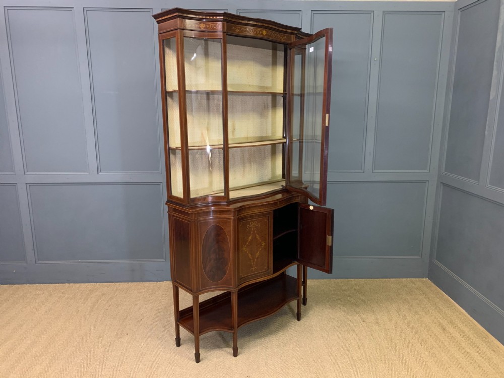 An Edwardian inlaid mahogany display cabinet featuring a glazed upper section, bow-front lower doors with marquetry panels, and tapered legs with a lower shelf. View XXVIII