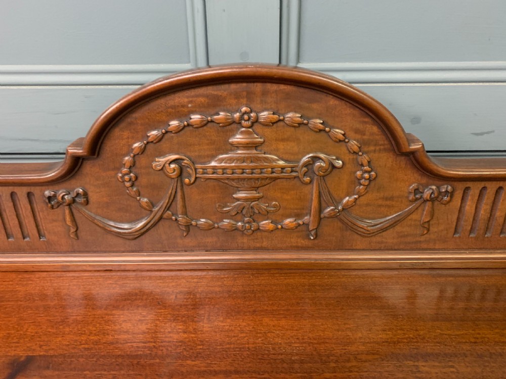 An Adam style mahogany side table featuring a carved upstand with an urn motif, relief drapery swags on the drawer fronts, and square fluted legs. View V