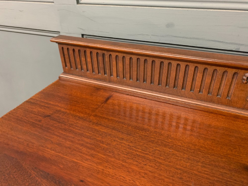 An Adam style mahogany side table featuring a carved upstand with an urn motif, relief drapery swags on the drawer fronts, and square fluted legs. View VI