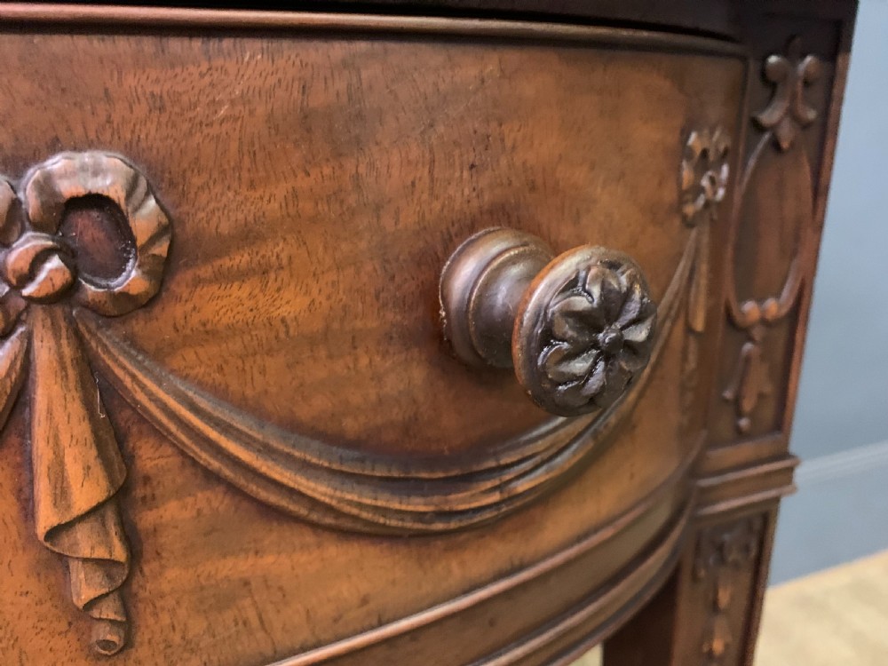 An Adam style mahogany side table featuring a carved upstand with an urn motif, relief drapery swags on the drawer fronts, and square fluted legs. View IX