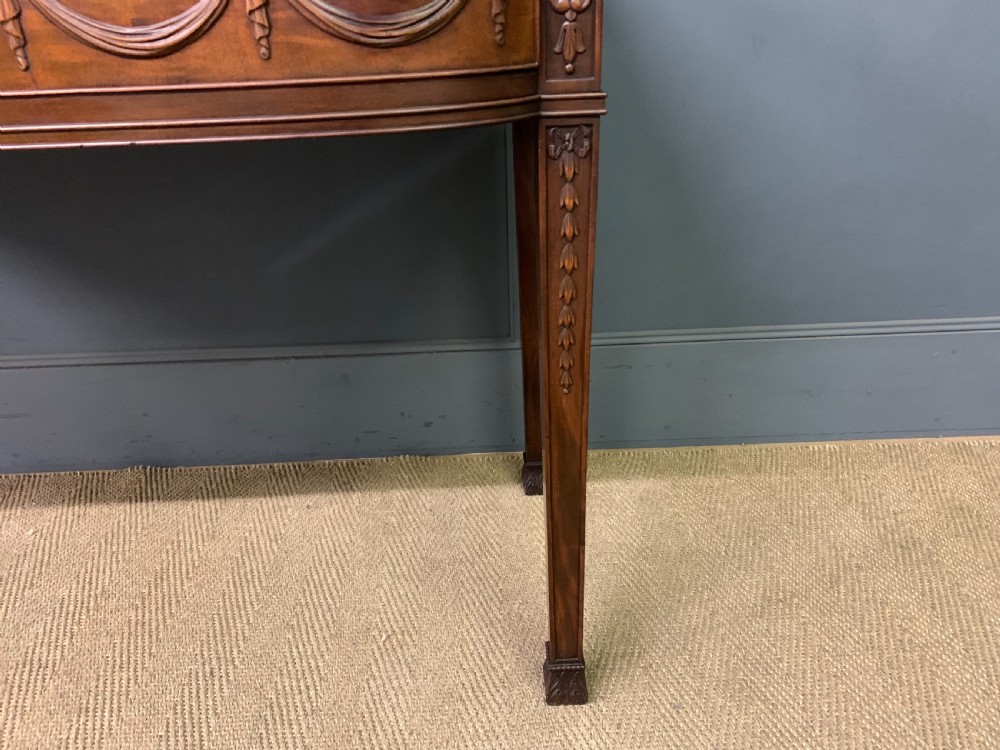 An Adam style mahogany side table featuring a carved upstand with an urn motif, relief drapery swags on the drawer fronts, and square fluted legs. View XI