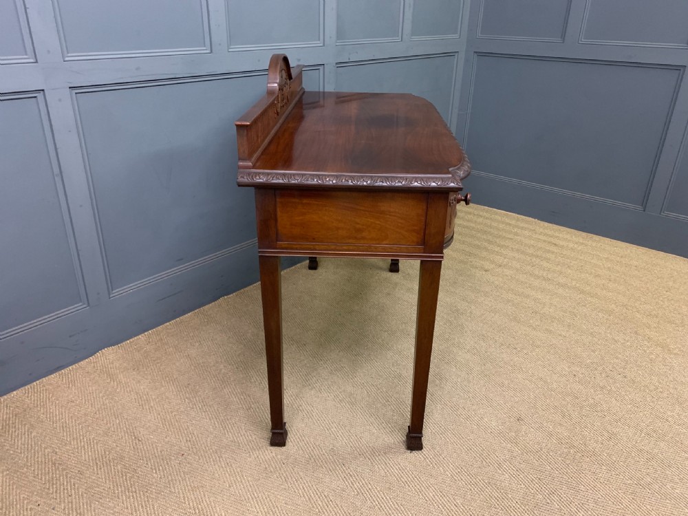 An Adam style mahogany side table featuring a carved upstand with an urn motif, relief drapery swags on the drawer fronts, and square fluted legs. View XIII