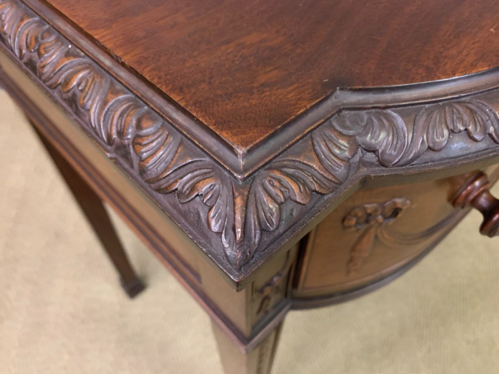 An Adam style mahogany side table featuring a carved upstand with an urn motif, relief drapery swags on the drawer fronts, and square fluted legs. View XV
