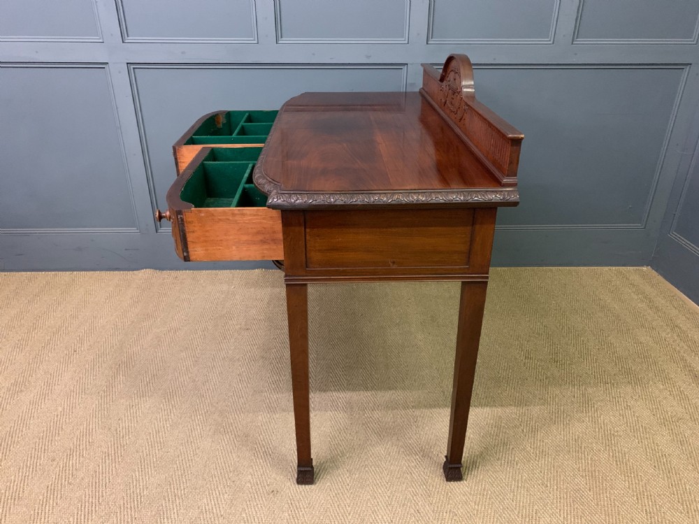 An Adam style mahogany side table featuring a carved upstand with an urn motif, relief drapery swags on the drawer fronts, and square fluted legs. View XIX