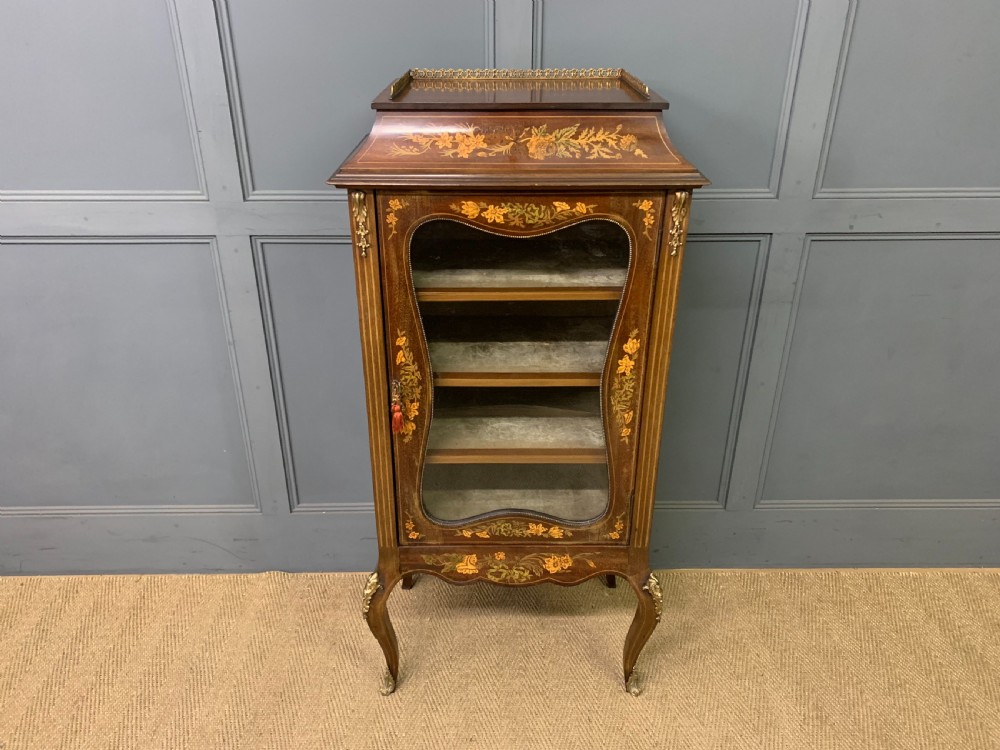 A freestanding mahogany vitrine featuring floral marquetry, a single glazed door, a brass top gallery, and cabriole legs with metal mounts.