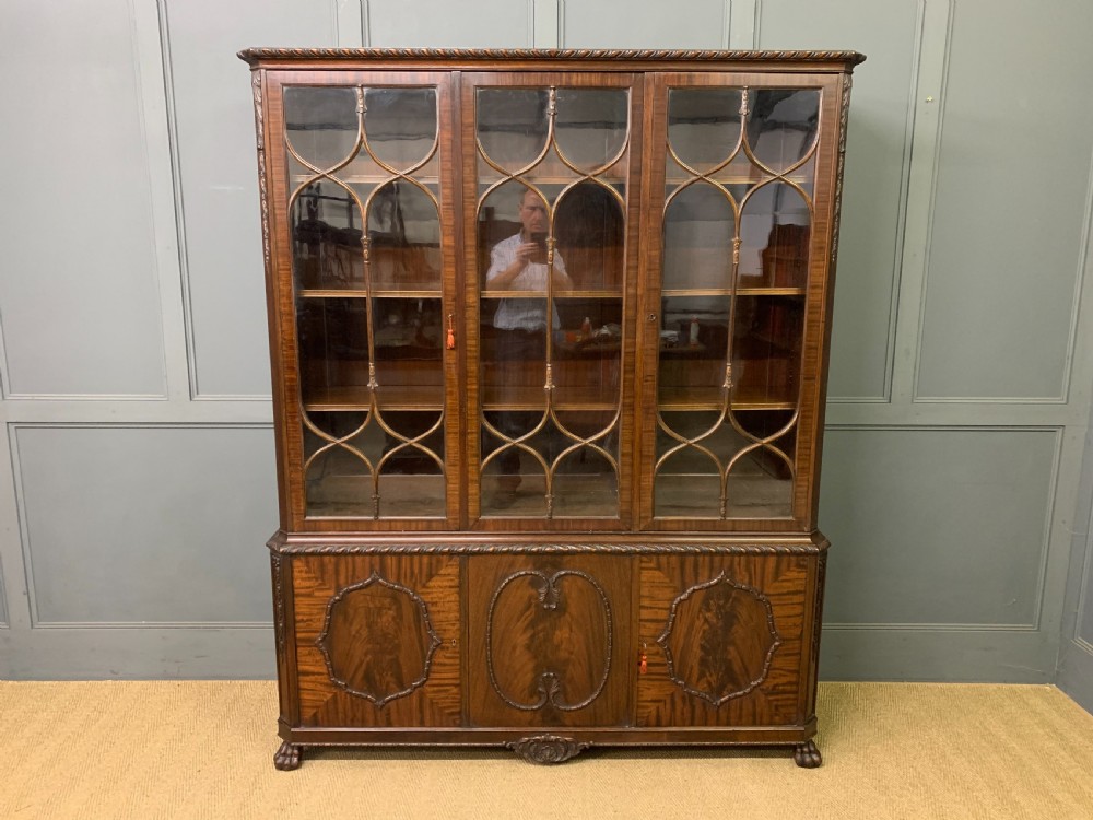 A tall mahogany Chippendale style glazed bookcase featuring three astragal glazed upper doors above three carved panelled lower cupboard doors resting on ball and claw feet. View II