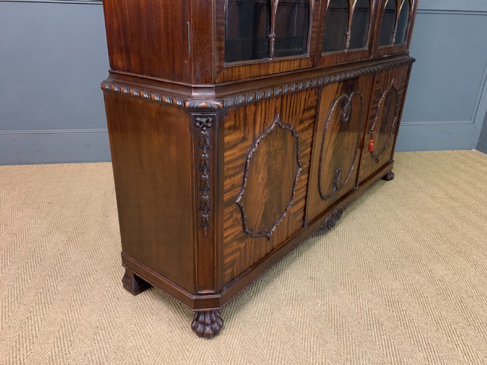 A tall mahogany Chippendale style glazed bookcase featuring three astragal glazed upper doors above three carved panelled lower cupboard doors resting on ball and claw feet. View VII