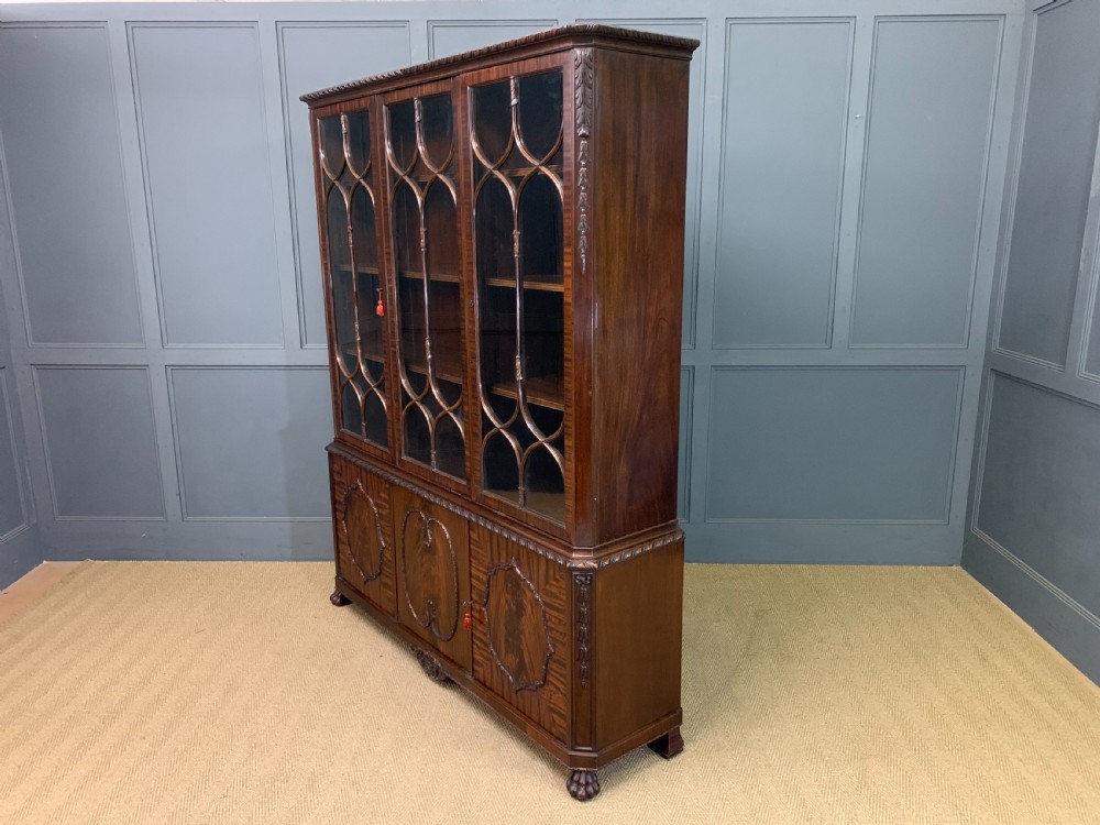 A tall mahogany Chippendale style glazed bookcase featuring three astragal glazed upper doors above three carved panelled lower cupboard doors resting on ball and claw feet. View IX