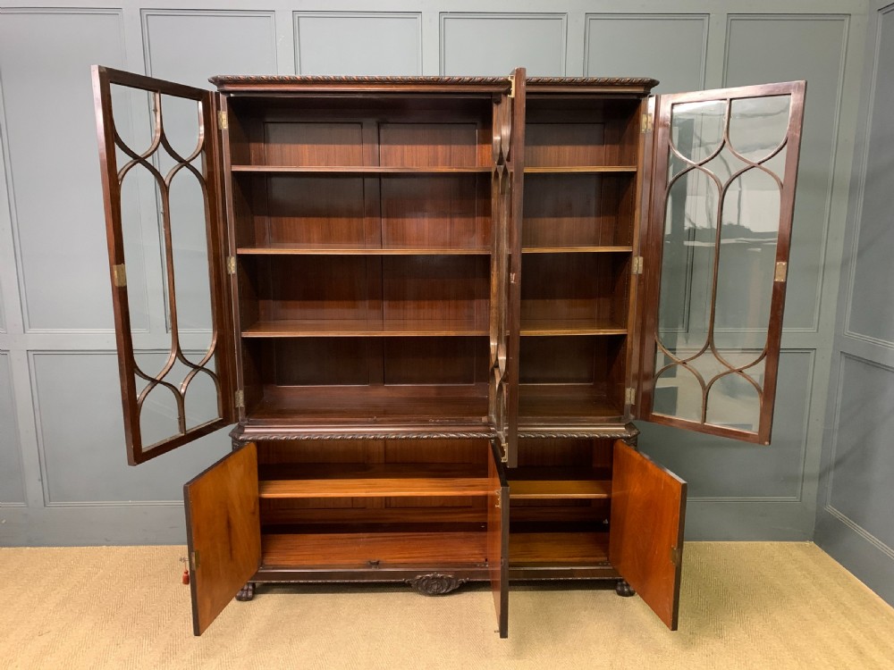 A tall mahogany Chippendale style glazed bookcase featuring three astragal glazed upper doors above three carved panelled lower cupboard doors resting on ball and claw feet. View X