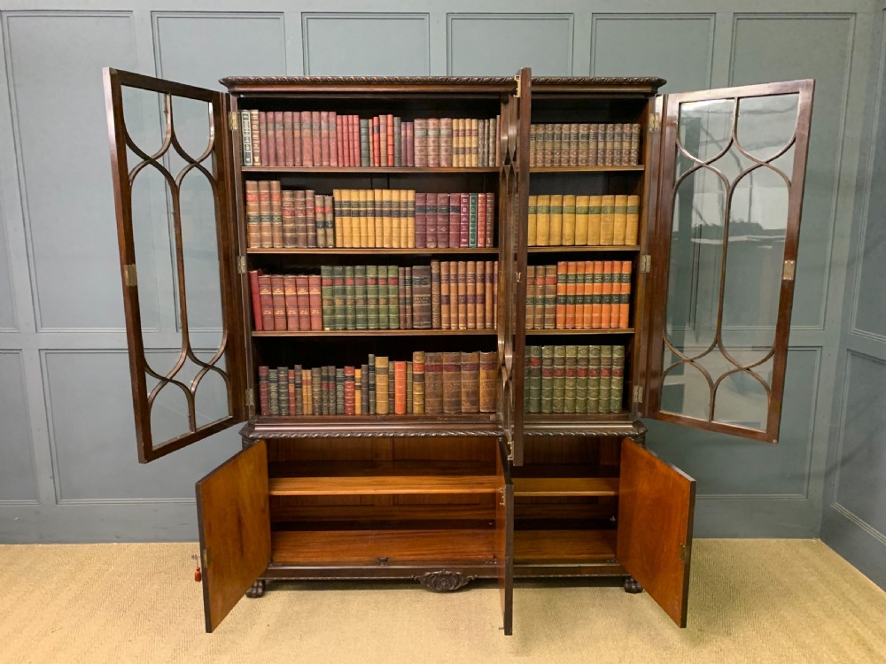 A tall mahogany Chippendale style glazed bookcase featuring three astragal glazed upper doors above three carved panelled lower cupboard doors resting on ball and claw feet. View XI
