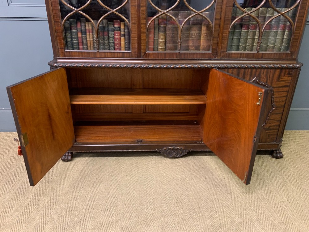 A tall mahogany Chippendale style glazed bookcase featuring three astragal glazed upper doors above three carved panelled lower cupboard doors resting on ball and claw feet. View XII