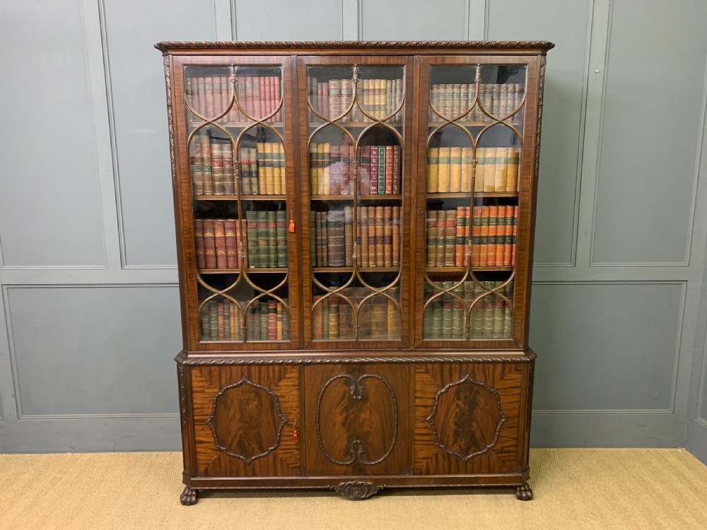 A tall mahogany Chippendale style glazed bookcase featuring three astragal glazed upper doors above three carved panelled lower cupboard doors resting on ball and claw feet. View XIII