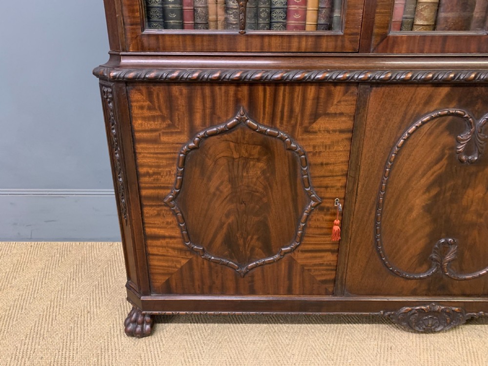 A tall mahogany Chippendale style glazed bookcase featuring three astragal glazed upper doors above three carved panelled lower cupboard doors resting on ball and claw feet. View XIV