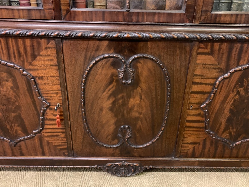 A tall mahogany Chippendale style glazed bookcase featuring three astragal glazed upper doors above three carved panelled lower cupboard doors resting on ball and claw feet. View XV